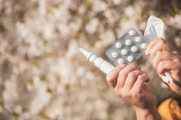 Mãos segurando uma cartela de comprimidos e um spray nasal