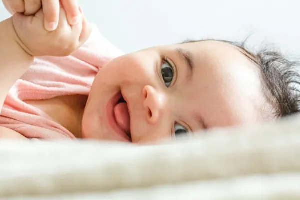 Bebê sorridente deitado sobre uma manta clara, em close do rosto