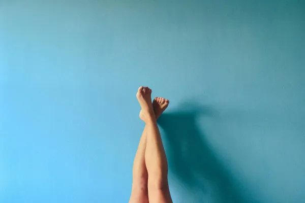 Pernas de uma pessoa cruzadas no ar diante de uma parede azul