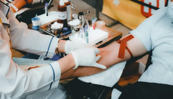 Profissional de saúde de luvas brancas coleta sangue do braço de um paciente