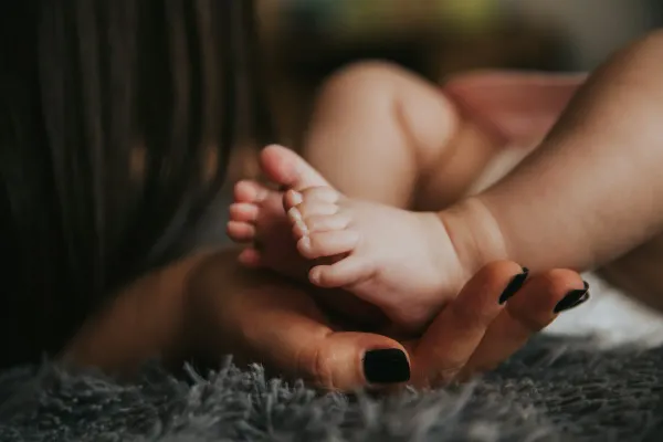 Pés de um bebê segurados pela mão da mãe sobre uma manta cinza