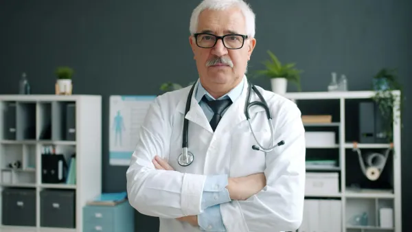 Médico experiente de jaleco branco e estetoscópio em pé no consultório