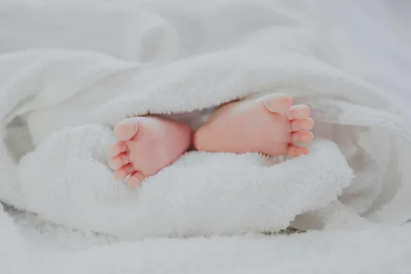 Pés de um bebê descalço aparecendo sob uma toalha branca