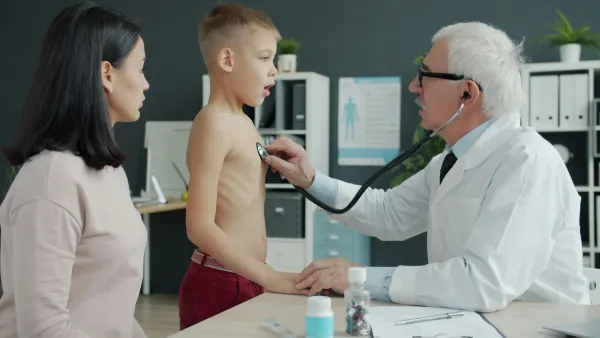 Médico ausculta o tórax de um menino com estetoscópio enquanto a mãe acompanha