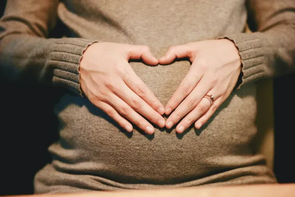 Gestante de suéter faz um coração com as mãos sobre a barriga