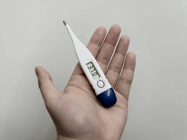 Mão segurando um termômetro digital clínico com leitura de temperatura
