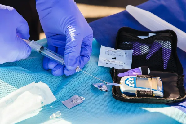 Mãos enluvadas coletam amostra de sangue para medir a glicemia no glicosímetro