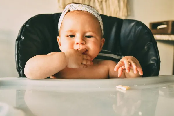 Bebê sentado na cadeirinha com a mão na boca