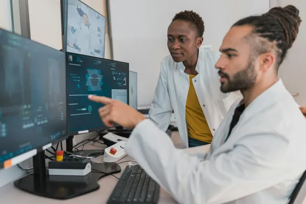 Dois médicos de jaleco analisam exames de imagem em monitores de computador