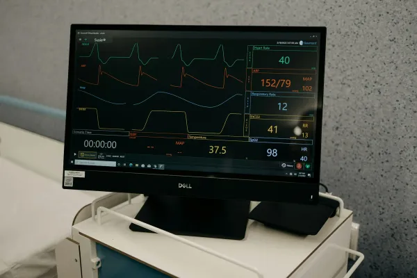 Monitor com traçados de ECG e sinais vitais sobre suporte em ambiente hospitalar