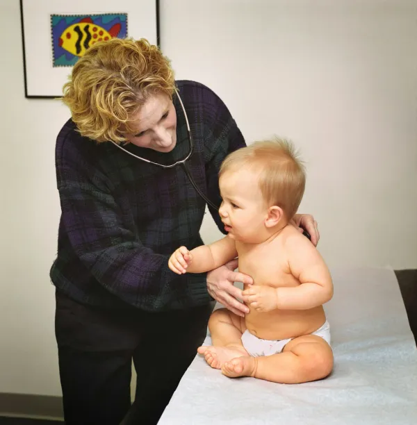 Pediatra segura um bebê sobre a maca durante a consulta