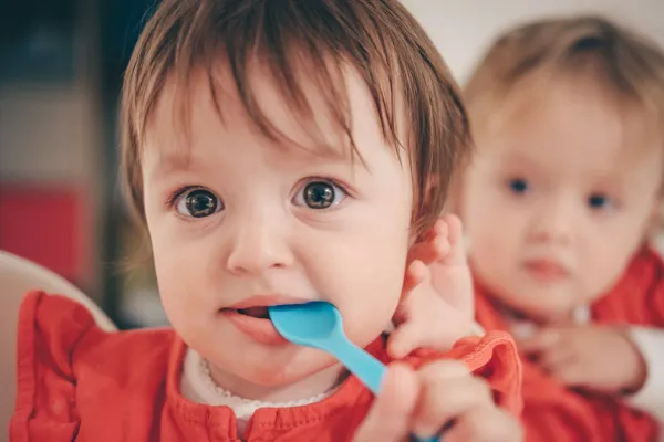 Criança pequena com uma colher azul na boca