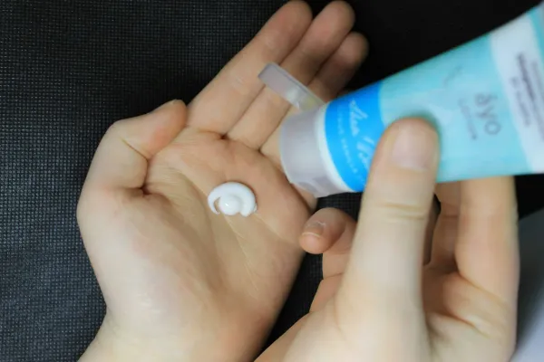 Mãos aplicando uma porção de creme hidratante na palma da mão