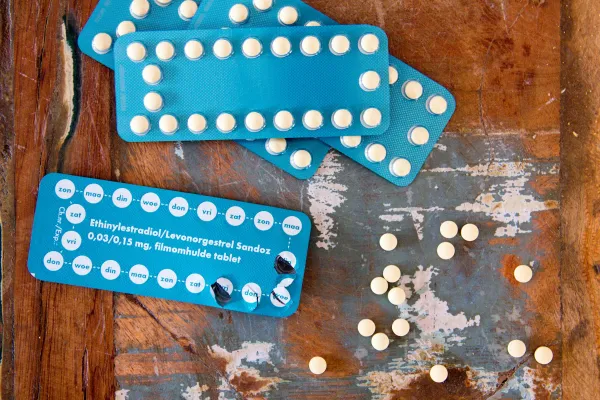 Cartelas azuis de contraceptivo oral e comprimidos espalhados sobre madeira