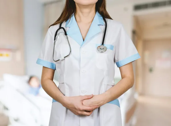 Profissional de saúde de uniforme branco e azul com estetoscópio no pescoço em corredor hospitalar